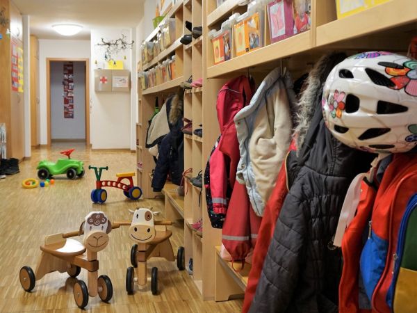 Das Bild zeigt den Eingangsbereich unserer Kleinkindgruppe. Es hängen Jacken in der Garderobe und auf dem Boden sind verschiedene Kinderfahrzeuge.