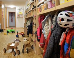 Das Bild zeigt den Eingangsbereich unserer Kleinkindgruppe. Es hängen Jacken in der Garderobe und auf dem Boden sind verschiedene Kinderfahrzeuge.