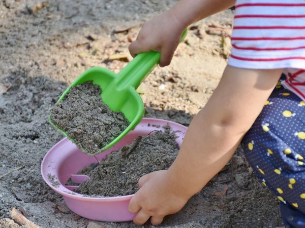 Ein kleines Kind spielt im Sandkasten mit einer grünen Schaufel und einem rosa Sieb.