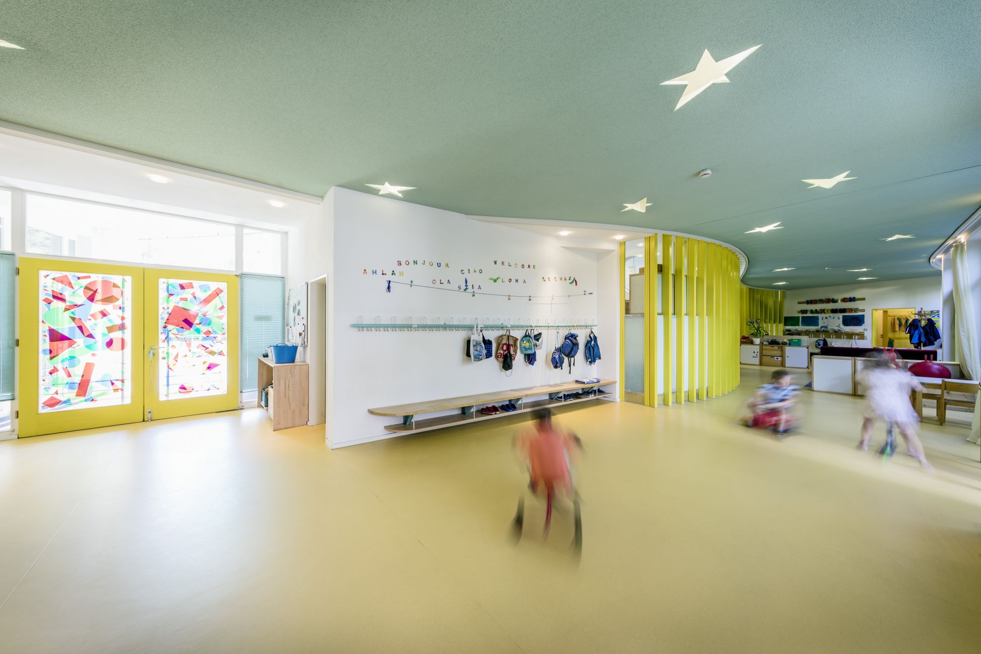 Der Eingangsbereich unserer Tagesgruppen in Petershausen mit der Eingangstür und einer Garderobe. Drei spielende Kinder sind auf dem Bild zu sehen.